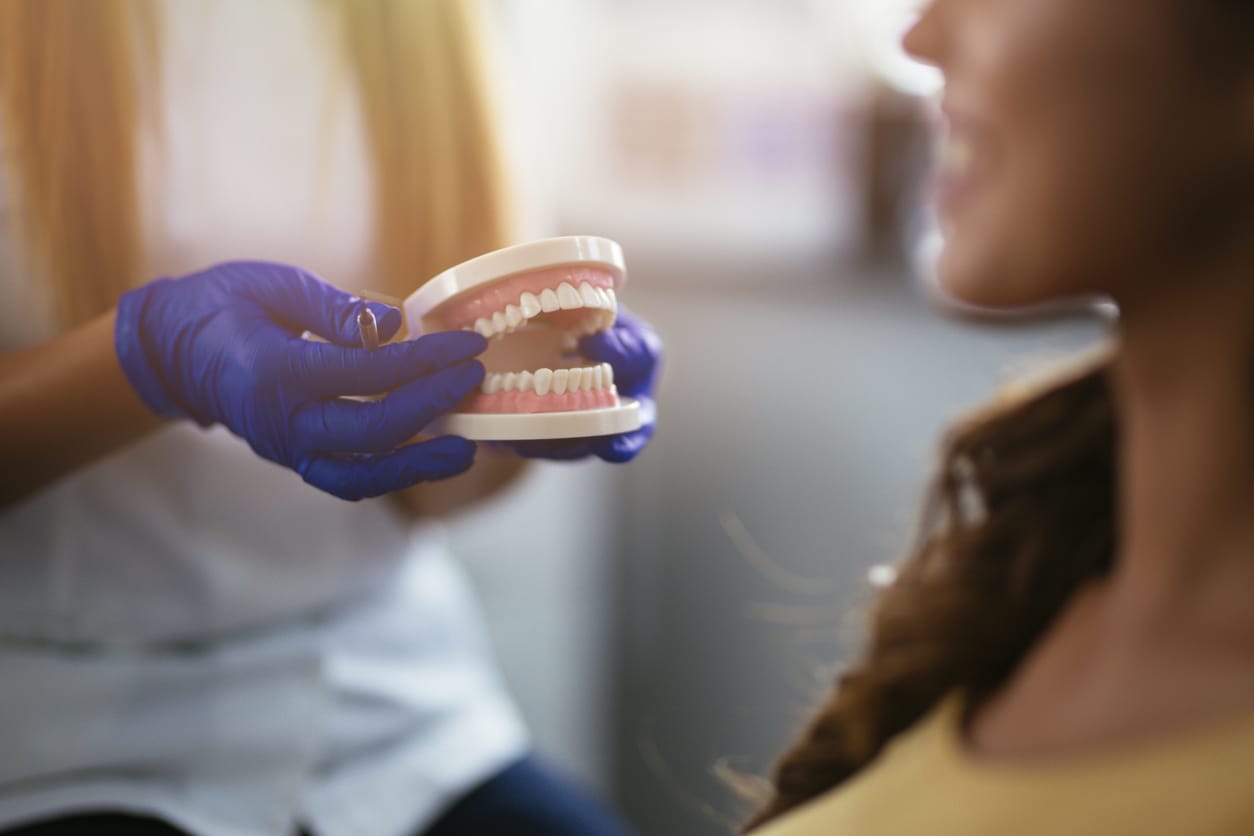 A dentist holding dentures discussing how to clean them with a dark-haired woman in a yellow shirt.