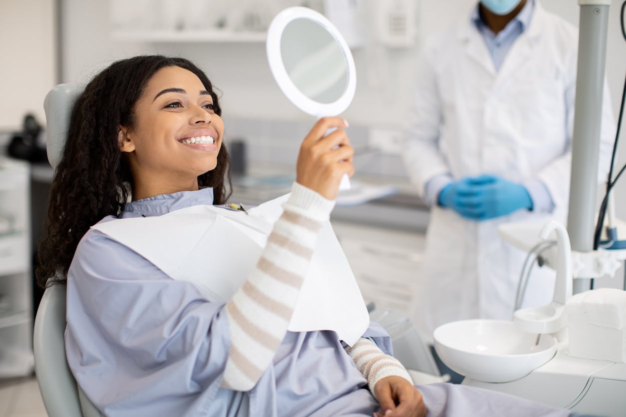 A happy female patient looking in the mirror after dental treatment.