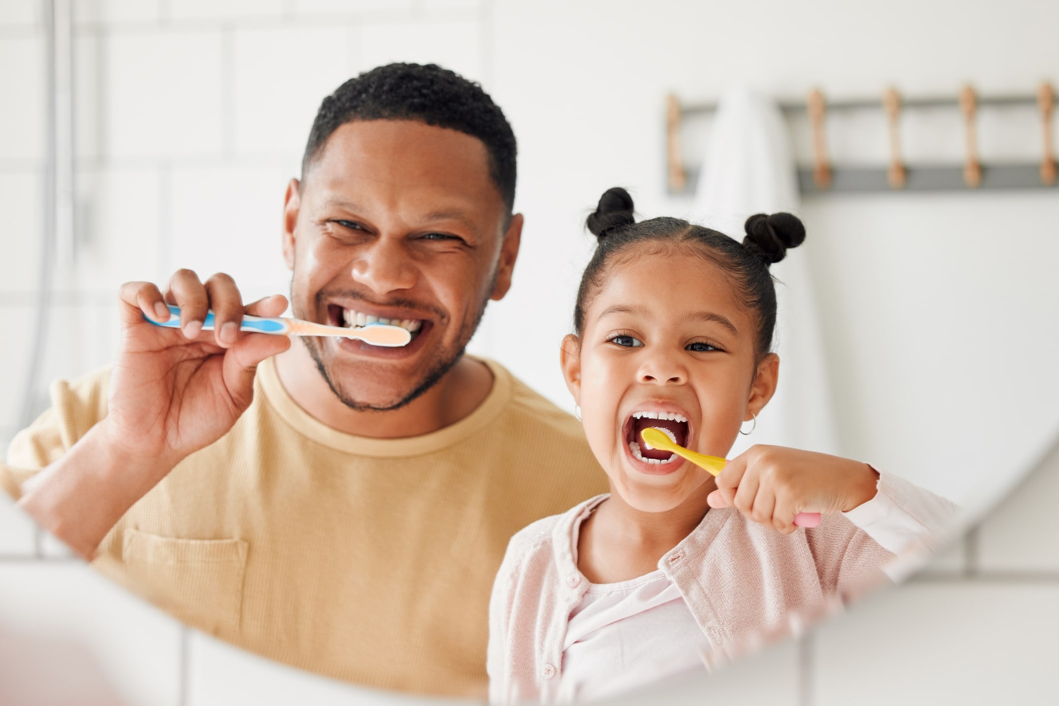 A father and daughter brushing their teeth together while looking in the mirror.
