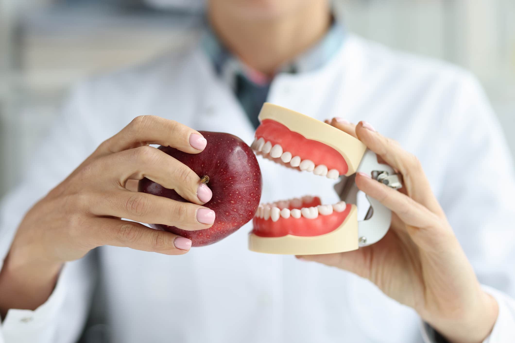 A dentist holding a pair of dentures and an apple to represent eating with dentures.