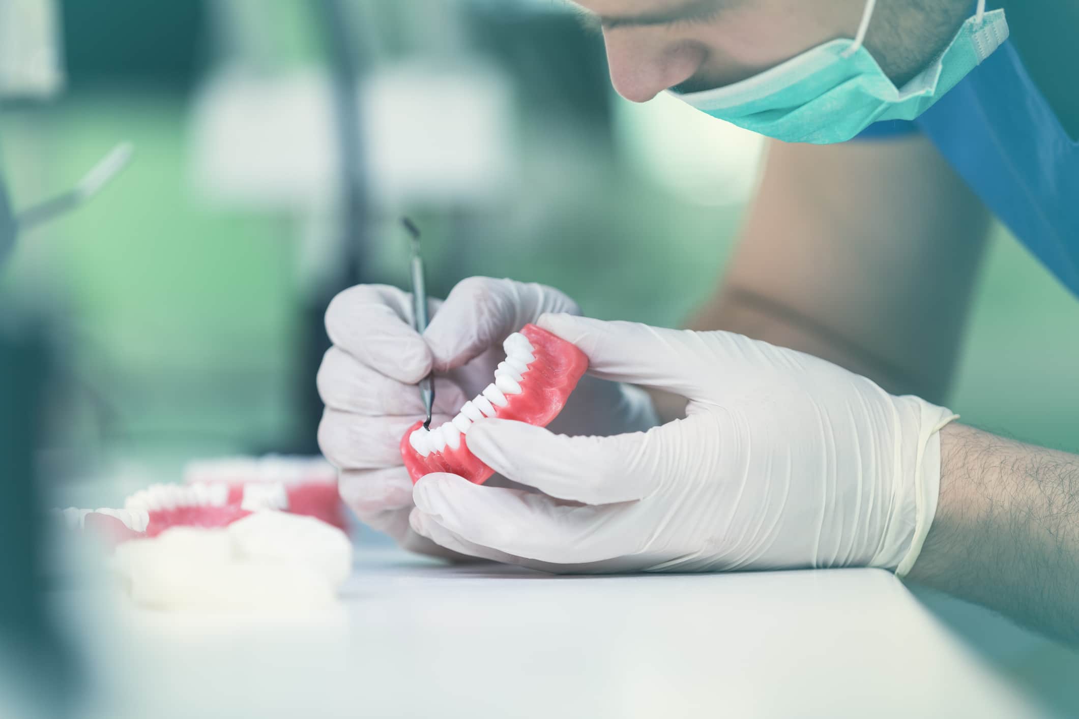 A dentist in white gloves working on a pair of implant-supported dentures.
