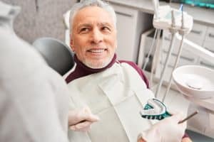 A man sits in a dentist’s chair as his provider takes a mold of his teeth for dental implants.