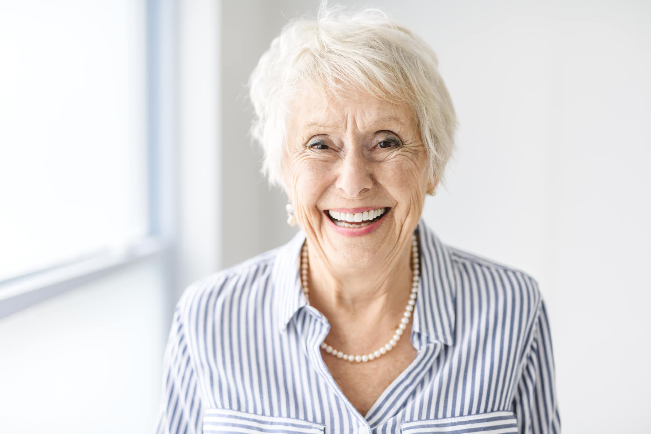 A woman with all on 4 dental implants smiles brightly in front of a white background.