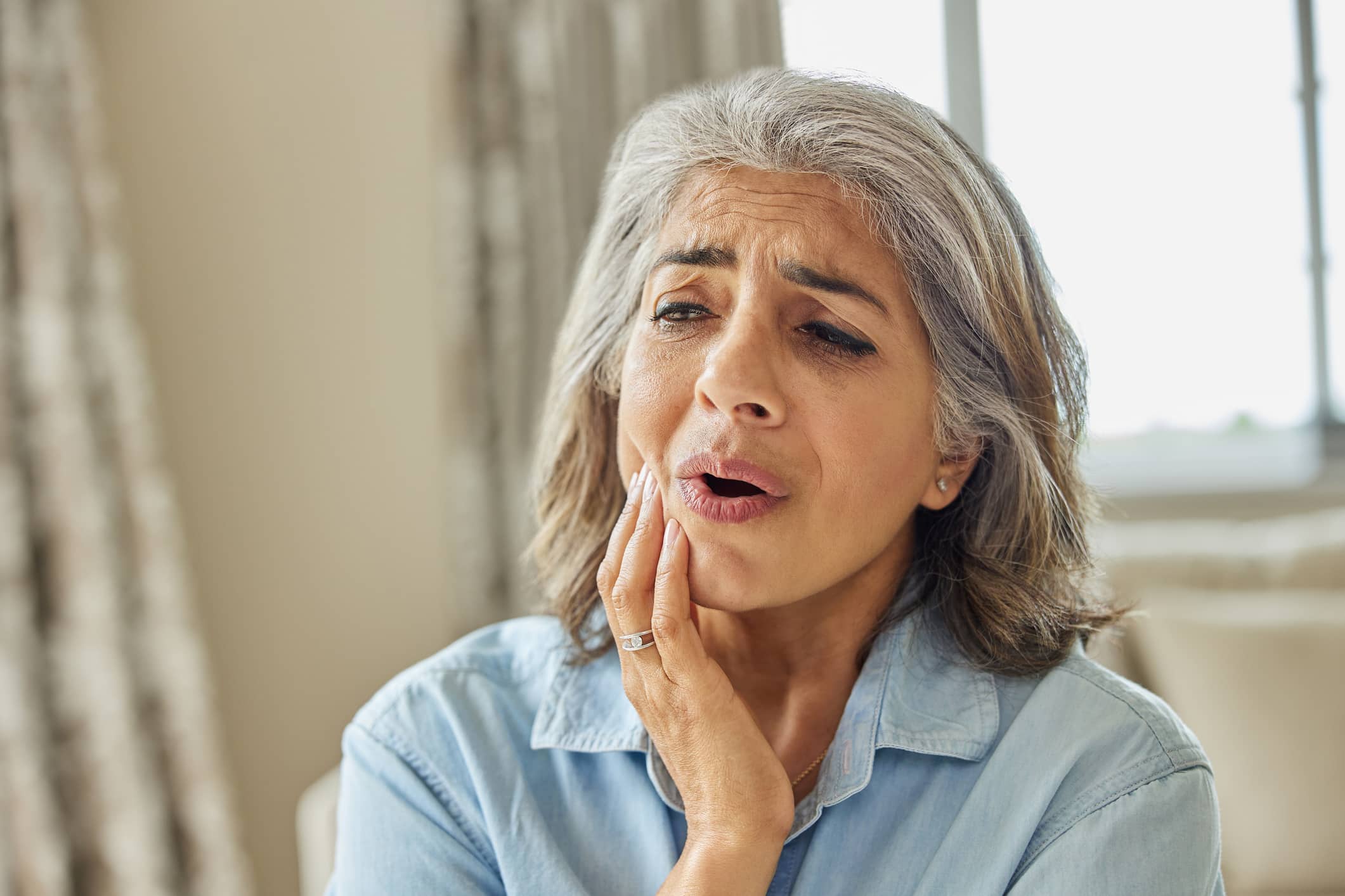 A woman with dentures holds her mouth in pain. It’s possible that dirty dentures have caused a mouth infection.